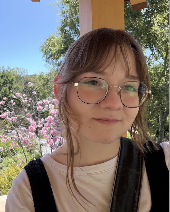 A picture of Gabby standing in front of a sunny sky and flowers.