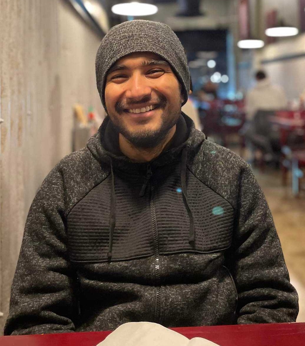 A picture of Sarthak Mishra sitting in a coat and hat.